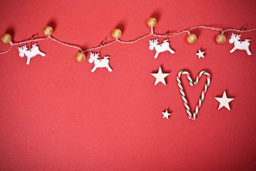 Christmas and New Year composition. Seasonal greeting card concept with white Christmas lights, reindeers and heart made of candy cane, on red background. Christmas, winter, new year concept. Flat lay, top view, copy space. 