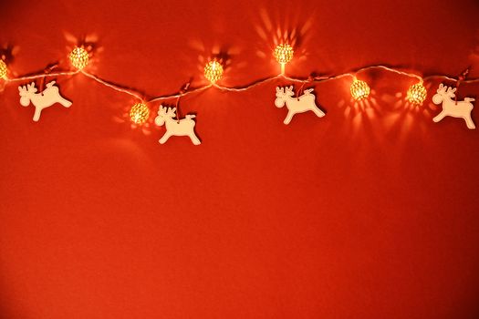 Christmas and New Year composition. Seasonal greeting card concept with Christmas lights and reindeers on red background. Christmas, winter, new year concept. Flat lay, top view, copy space. 