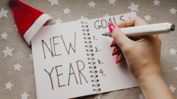 Notebook is with New year goals text with hand on christmas background
