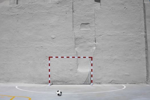 Soccer ball and goal with net against plastered wall background. Football at school yard scenery