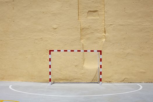 Soccer ball and goal with net against plastered wall background. Football at school yard scenery