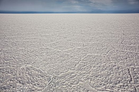 A low angle view of cracked salt flat in Salar de Uyuni, Potosi region, Bolivia. The weather is clear with blue sky.