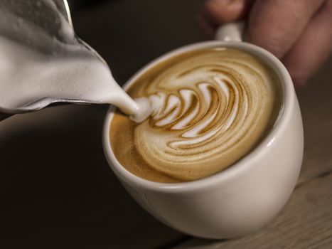 Close up hand of barista making latte or cappuccino coffee pouring milk making latte art