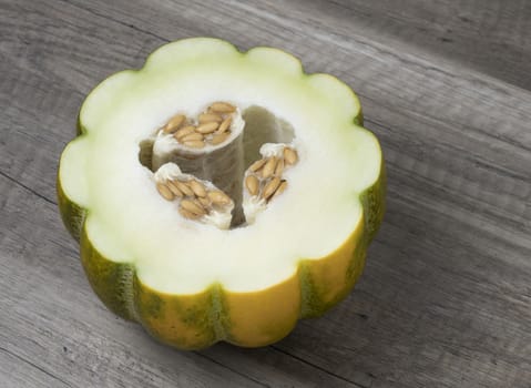 Half of ripe fresh melon with seeds isolated on wooden background. Sweet tropical fruit.
