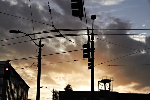 High-voltage electricity wires and traffic lights silhouetted against sunset.