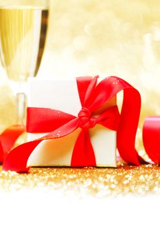 Champagne glasses and present in whitebox with red ribbon on golden background