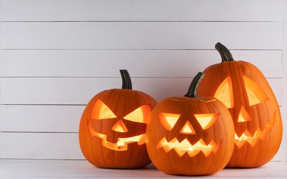 Three Glowing Halloween pumpkins head jack lantern on white wooden background