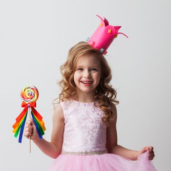 Beautiful little candy princess girl in crown holding big lollipop and smiling