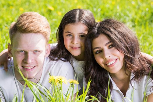 Portrait of happy family of parents and daughter laying down in grass