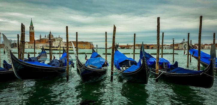 An enchanting view of the lagoon of Venice with four gondolas in the foreground and the storm behind it. Panoramic Image at 16:9.