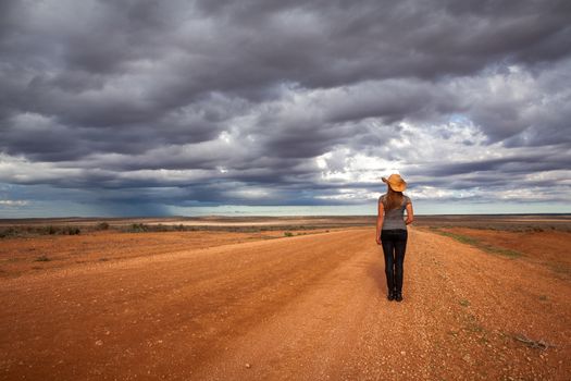 Farm girl watches the storm over an arid desert landscape of outback Australia