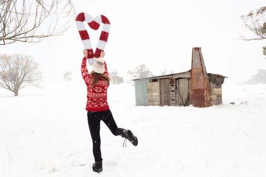 Happy joyous woman holding red and white candy canes in the shape of a heart in a snow covered rural landscape