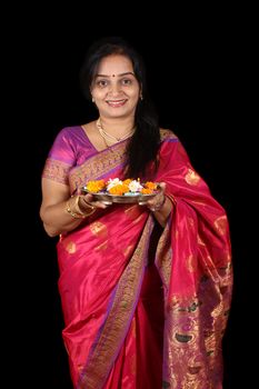 A beautiful middle aged Indian woman smiling happily while holding a traditional plate of Hindu rituals for Diwali festival in India.
