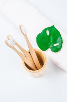 Bamboo toothbrushes in wooden glass with towel. Eco friendly concept.