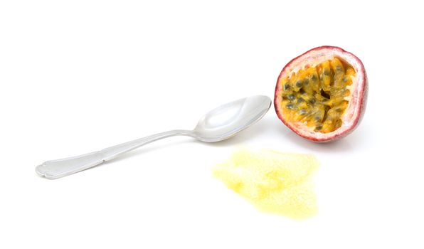 Half passion fruit showing yellow pulp and seeds, with spilled juice and silver spoon, on a white background 