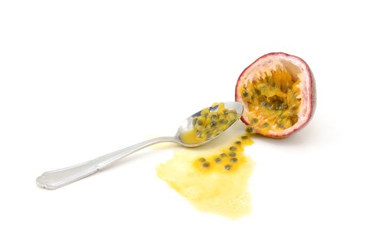 Scooping out pulp from half a passion fruit with a spoon, spilled seeds and juice, on a white background