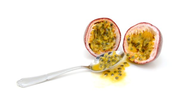 Spoon scooping out pulp and seeds from a purple passion fruit cut in half, on a white background