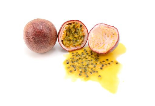 Whole and halved purple passion fruits with spilled juice and sweet seeds, on a white background 