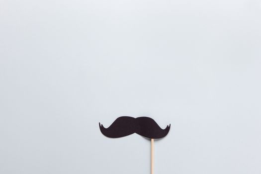 Accessory in form of black moustache on stick on grey background with place for text. Concept men's health, prostate cancer awareness month, no shave, charity, Father's Day. Horizontal. Flat lay.