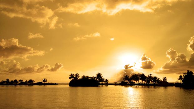 Golden sunset  with silhouettes on a tropical beach at sunset in Maldives