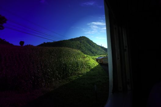 View from train railway makes a curve bend through beautiful natural green grasslands and mountains . Travel in Thailand ,Effect saturation