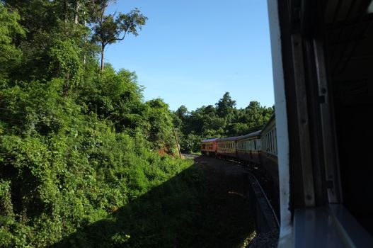 View from train railway makes a curve bend through beautiful natural green grasslands and mountains . Travel in Thailand