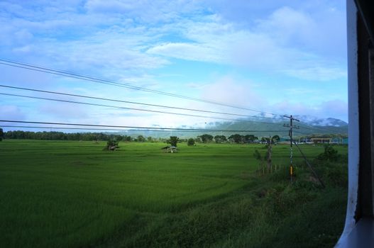 View from train window in motion of countryside and sky on sunny warm , in Thailand , 