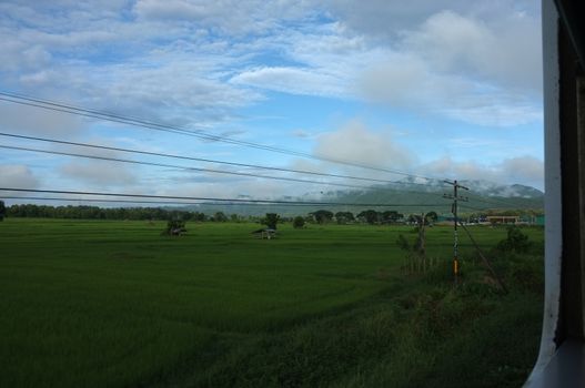 View from train window in motion of countryside and sky on sunny warm , in Thailand , 