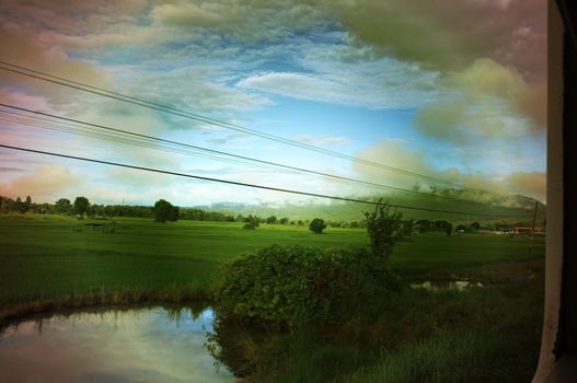 View from train window in motion of countryside and sky on sunny warm , in Thailand , 