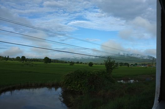 View from train window in motion of countryside and sky on sunny warm , in Thailand