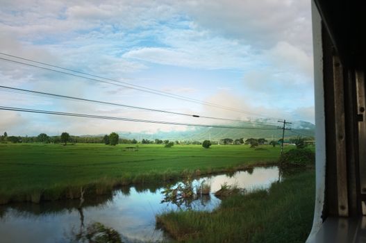 View from train window in motion of countryside and sky on sunny warm , in Thailand , 