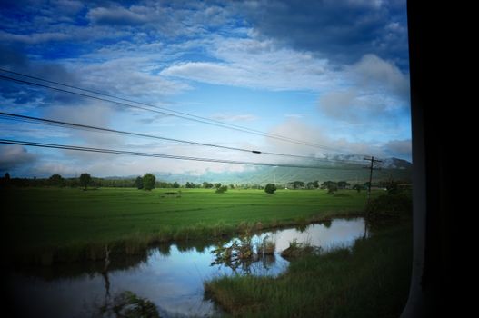View from train window in motion of countryside and sky on sunny warm , in Thailand , 