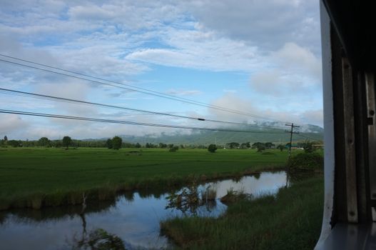 View from train window in motion of countryside and sky on sunny warm , in Thailand , 
