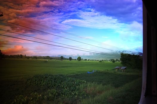 View from train window in motion of countryside and sky on sunny warm , in Thailand , Effect saturation