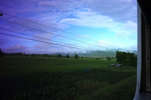 View from train window in motion of countryside and sky on sunny warm , in Thailand , 