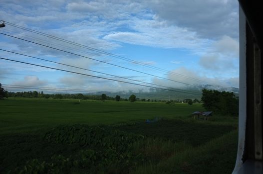 View from train window in motion of countryside and sky on sunny warm , in Thailand , 