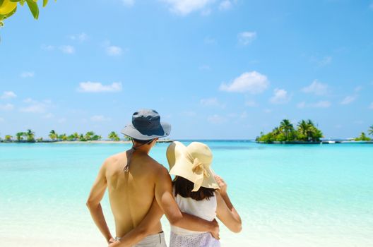 Young happy asian couple  in sunhat on white beach at summer vacation in Maldives island