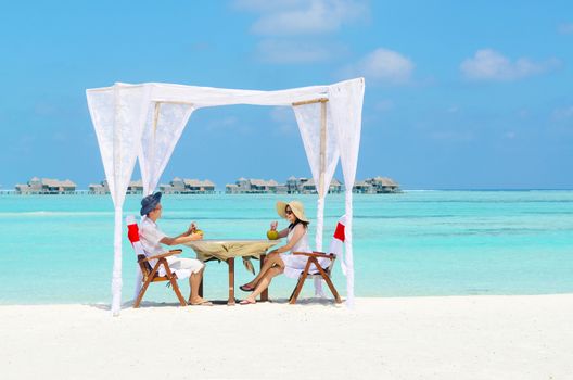 Asian couple in sunhat enjoying romantic luxury lunch setting at tropical beach in Maldives