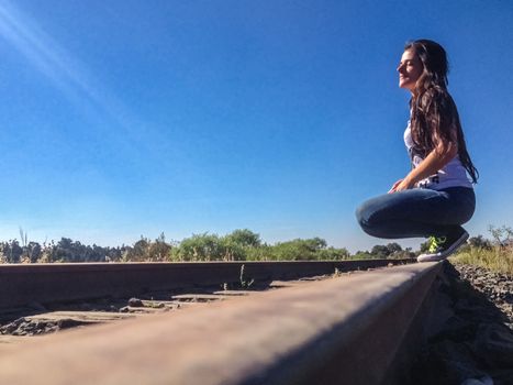 Beautiful latin woman sitting on the train tracks on a clear day