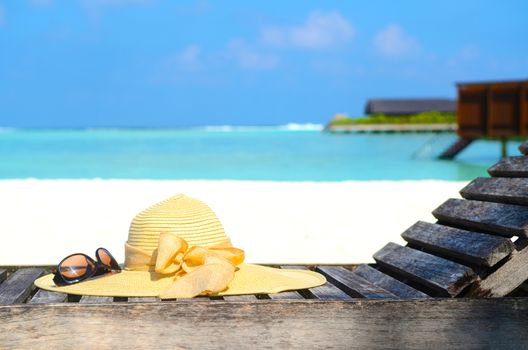 Deckchairs with sunhat and sunglass on jetty in front of tropical resort at maldives island