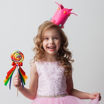 Beautiful little candy princess girl in crown holding big lollipop and smiling