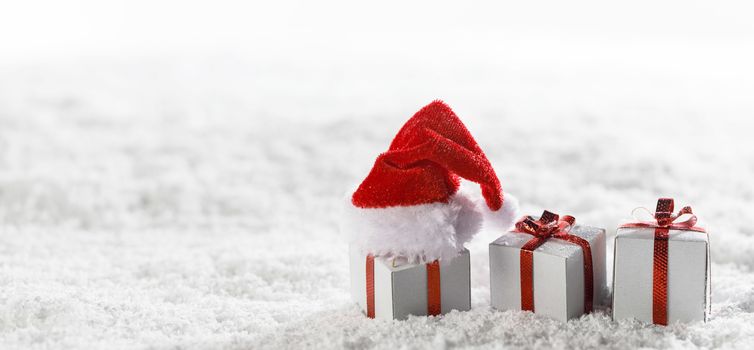 Christmas holidays card with small gifts and santa claus hat in snow
