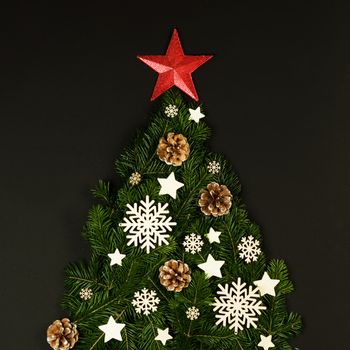 Christmas tree made of natural spruce branches deecor with red star on black background, flat lay card with copy space