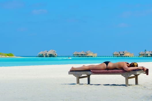 Woman relaxing and sunbathing on beach at tropical maldives island.