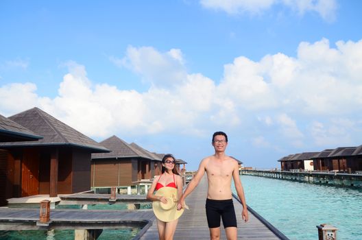 Asian couple on a tropical beach jetty at villa water resort,Maldives