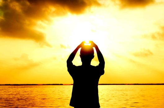 man's hands forming a heart shape with sunset silhouette at tropical beach,maldives island .