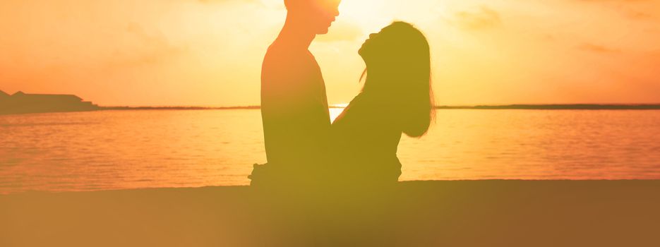 Loving asian couple on the beach, drinking wine at sunset, silhouettes.
