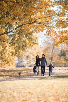 Happy smiling family of parents and children walking with dog together holding hands in autumn park