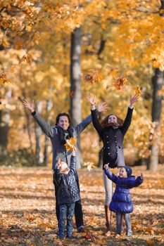Happy smiling family of parents and children playing throwing leaves in autumn park