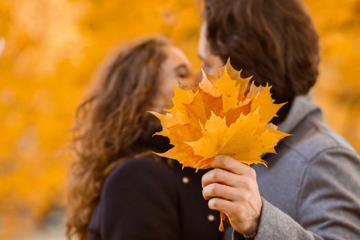 love, relationship, family and people concept - couple with maple leaves kissing in autumn park